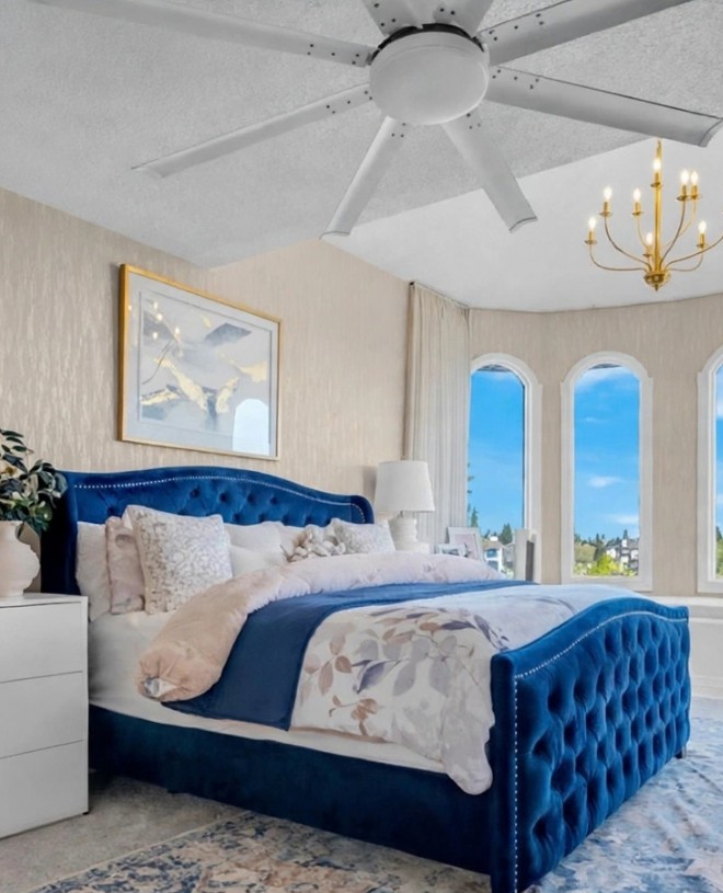 Bedroom with freshly installed textured wallpaper, a blue tufted bed and arched windows